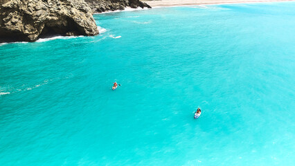 Aerial view of family supboarding. Mom and dad oaring on paddleboards with their sons down azure sea