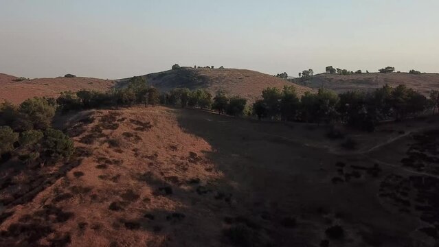 aerial footage of majestic mountain ranges covered in dry brush and lush green trees and plants with blue sky at sunset at Puddingstone Lake in San Dimas California USA