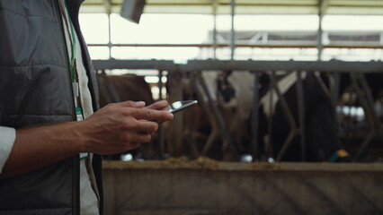 Obraz na płótnie Canvas Farmer hands holding tablet computer closeup. Livestock owner walking cowshed.