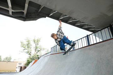 Portrait of teenage boy riding skateboard and doing tricks jumping in air at skatepark outdoors