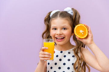 A little girl holds a glass of orange juice and a slice of orange, freshly squeezed juice for breakfast, natural vitamins for children.