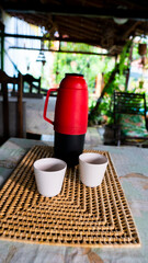 red bottle with coffee and two cups, on the table in a peaceful day.