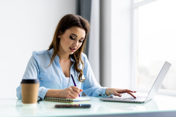 Business woman work on computers and write on notepad with pen to calculate financial statements within the office.