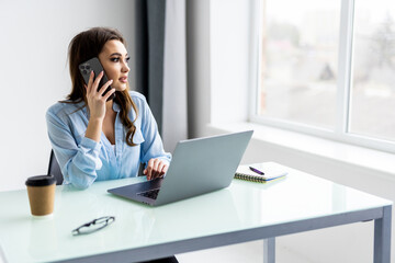 Portrait of beautiful executive woman making call while sitting at her workplace in front of laptop and working on new project.