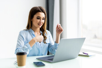 Young business woman making video call with computer while talking with earphone sitting in modern startup office.