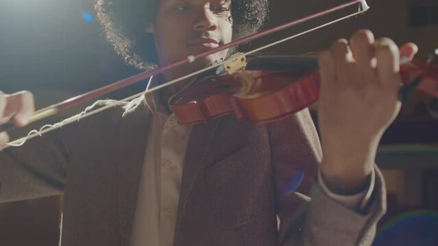 Low angle shot of young African American musician playing violin during rehearsal in concert hall