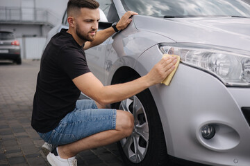 Hand of man wipes headlight of his car using rug. Self-service car wash. Outdoor