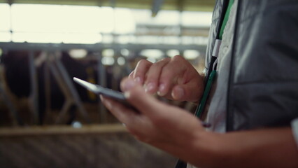 Closeup farmer hands using tablet computer in modern dairy farm facility cowshed