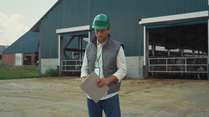 Livestock supervisor making notes holding clipboard at modern cowshed building.