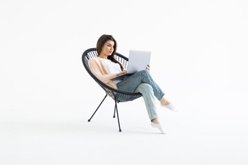 Portrait of a young businesswoman sitting in a chair with laptop computer against white background