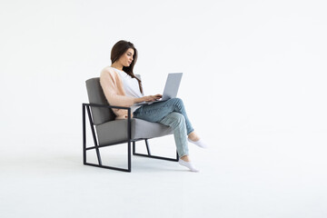 Portrait of a young businesswoman sitting in a chair with laptop computer against white background