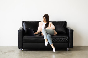 Photo of woman smiling and using laptop while sitting on couch in bright room