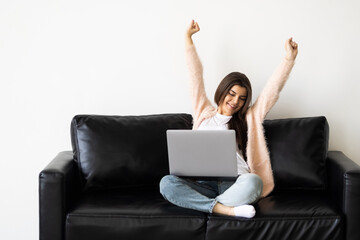 Overjoyed young woman sit on couch at home triumph receive pleasant email or read good news on laptop online