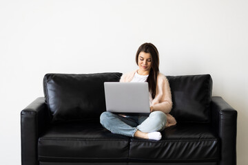 Fototapeta na wymiar Smiling young woman using laptop, sitting on couch at home