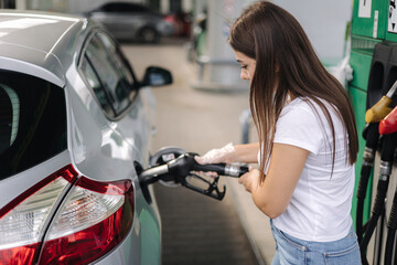 Fototapeta na wymiar Attractive young woman refueling car at gas station. Female filling diesel at gasoline fuel in car using a fuel nozzle. Petrol concept. Side view. Fuel shortage in Ukraine