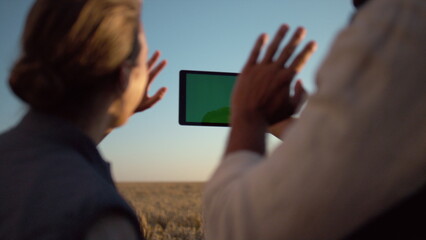 Couple holding chroma key pad computer at cultivated grain harvest sunlight.