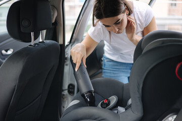 Close-up of female using portable vacuum cleaner in her car. Baby ca seat cleaning. Woman vacuuming...