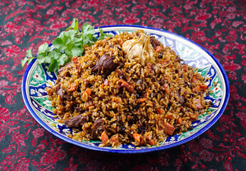 Traditional Uzbek fergana plov with devsira rice and lamb meat served as close-up on a handmade painted lagan platter
