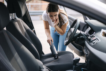 Woman vacuuming her car in the garage at home. Female using portable vacuum cleaner to remove dust...