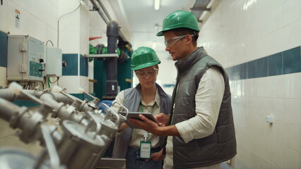 Factory engineers check equipment in compartment. Supervisors talk at machinery