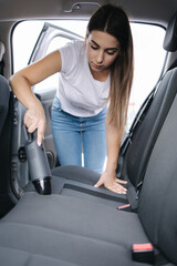 Attractive young woman using portable vacuum cleaner in her car. Woman vacuuming her car in the...