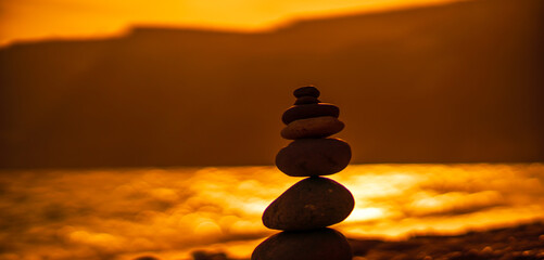 Pebble pyramid silhouette on the beach. Sunset with sea in the background. Zen stones on the sea beach concept, tranquility, balance. Selective focus