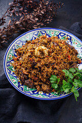 Traditionelles usbekisches Fergana Plov mit Devsira Reis und Lammfleisch serviert als close-up auf einer handgefertigten bemalten Lagan Platte