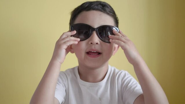 Little boy wear adult's sunglasses on colour background