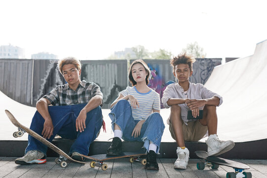 Full length portrait of three tenagers in satepark sitting on ramp and looking at camera urban setting