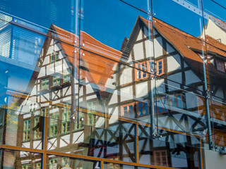 Obraz premium Ein Fachwerkhaus spiegelt sich in der verglasten Fassade eines Gebäudes im Sonnenschein