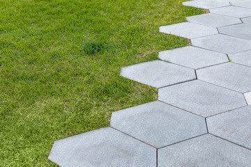 The border between the green grass and the large paving slabs of the pedestrian path. Infrastructure of the park, landscaping of the infield, residential area