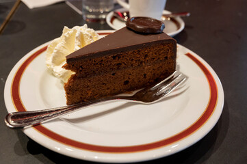 Piece of famous Sachertorte chocolate cake with apricot jam of Austrian origin served with whipped cream