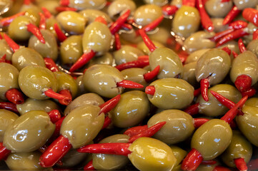 Green fresh olives with chili pepper close up on market, food background