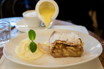 Austrian sweet dessert, portion of apple strudel with whippen cream and hot vanilla sauce served in old bakery cafe in Vienna, Austria