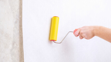 Fototapeta na wymiar A man rolls out a canvas of white wallpaper with a suture yellow roller. Removing air bubbles and glue. Wallpapering. Repair of a room, apartment, house.
