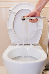 A male plumber repairs the hygienic shower head in the bathroom.