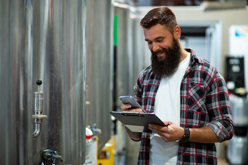 Man working in brewery and taking notes of the beer production and using smartphone