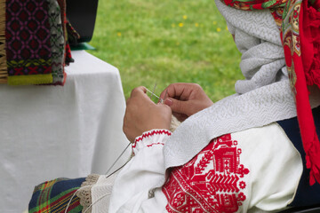 Woman in a national costume knits with needles. Selective focus.