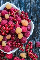 Yellow and red organic raspberry mixed with red currant. The bowl with fresh berries is placed on natural wood. Healthy snack and tasty dessert