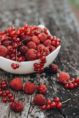 White bowl with fresh organic raspberry and red currant. Placed on  natural gray wood background. Tasty snack or fresh topping for your desserts
