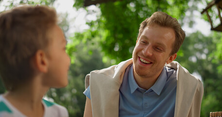 Munching boy laughing talking with father on picnic. Family lunching in park. 