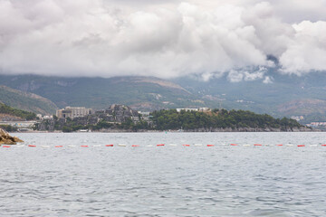 Obraz premium Budva, Montenegro - August 26, 2021: View of Budva town, Luxury travel destination with beatuiful beaches at Adriatic sea with amazing mountainscape covered in clouds