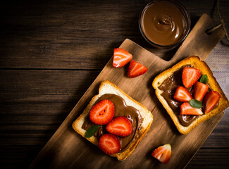 Toasted bread with chocolate spread strawberries on a wooden background