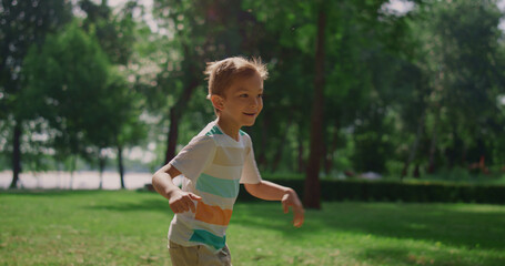 Happy boy running in green park. Joyful kid playing catch-up on weekend outdoors