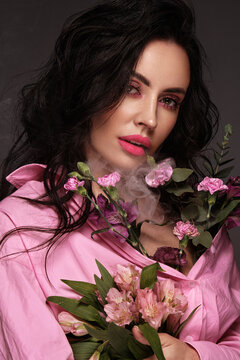 Beautiful brunette girl iwith a gentle pink romantic make-up, pink lips, holding flowers. The beauty of the face.