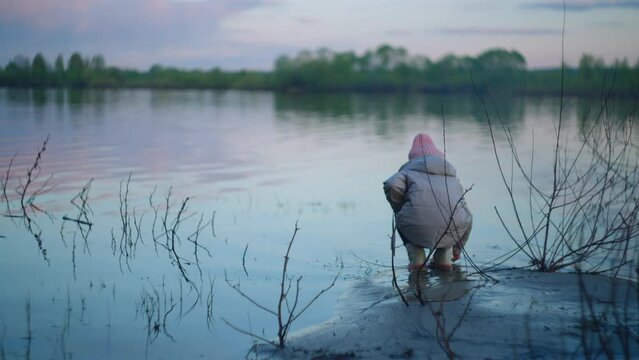Lonely girl look at the water in the pond standing alone. Slow motion lonely girl is sad looking at the river