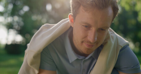 Closeup happy blond man look down in park. Handsome guy pose in golden sunlight