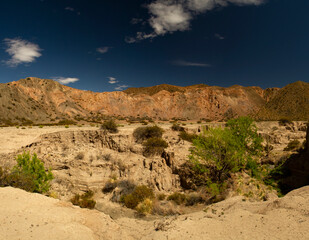 Arid environment. Panorama view of the sandstone cliffs, canyon, rocky mountains and desert sand, under a deep blue sky.