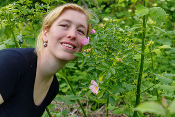 Lächelnde Frau mit rosa Wildrosen im Garten