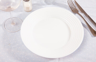 Clean empty ceramic plate with knife and fork on a tablecloth in a restaurant
